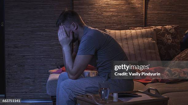 side view of man suffering from headache while sitting on sofa - man headache stock pictures, royalty-free photos & images