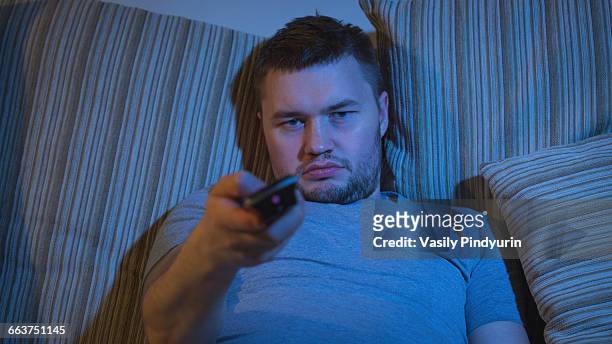 portrait of man watching tv while resting on sofa - people watching at camera stock-fotos und bilder