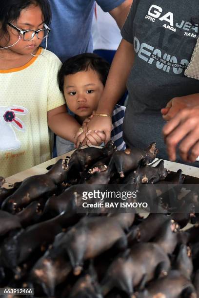 This picture taken on February 18, 2017 shows children watching as a vendor prepares bat meat for his customers in Tomohon market in northern...