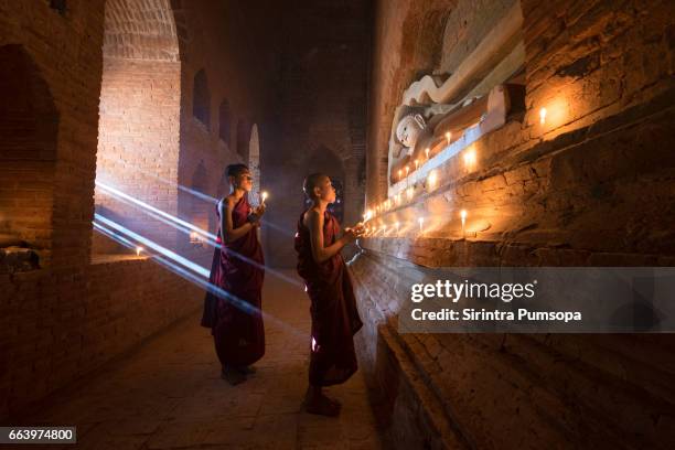 young buddhist monk praying with candles inside pagoda of old bagan, mandalay, myanmar - bagan stockfoto's en -beelden