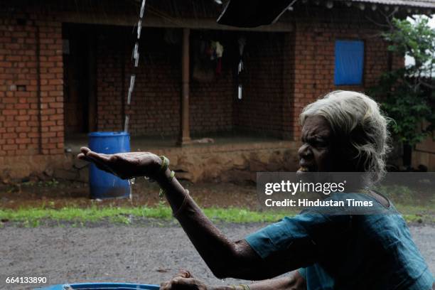 Baiji Devji Surum in Thane's Dongripada village, examining rain water collecting in her big blue drum in Mumbai, India.