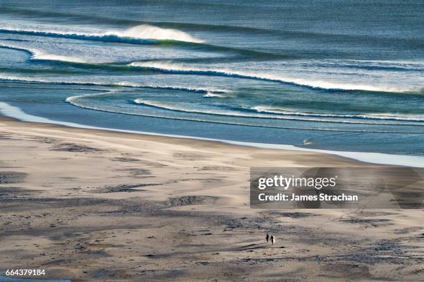 two silhouetted surfers returning across the beach, surf in background, surfboard glinting, nordhoek bay, cape town, south africa - noordhoek beach stock pictures, royalty-free photos & images