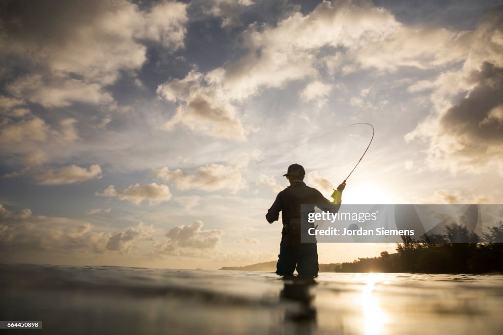A man fly fishing in the ocean.