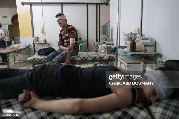 Syrian men receive treatment at a makeshift clinic following reported air strikes by government forces in the rebel-held town of Douma, on the...