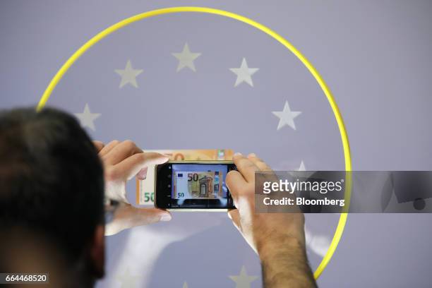An attendee uses a smartphone to photograph a new 50 euro currency bank note during its unveiling at the European Central Bank headquarters in...