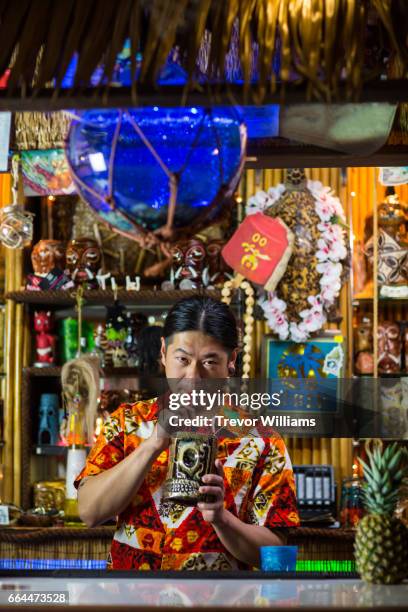 mid adult man sipping a drink in a tropical themed drinking establishment - bar drink establishment stock pictures, royalty-free photos & images