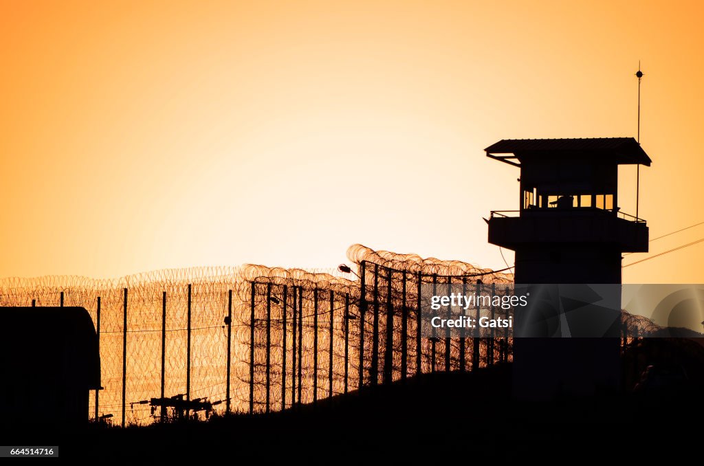 Silhouette of barbed wires and watchtower of prison.