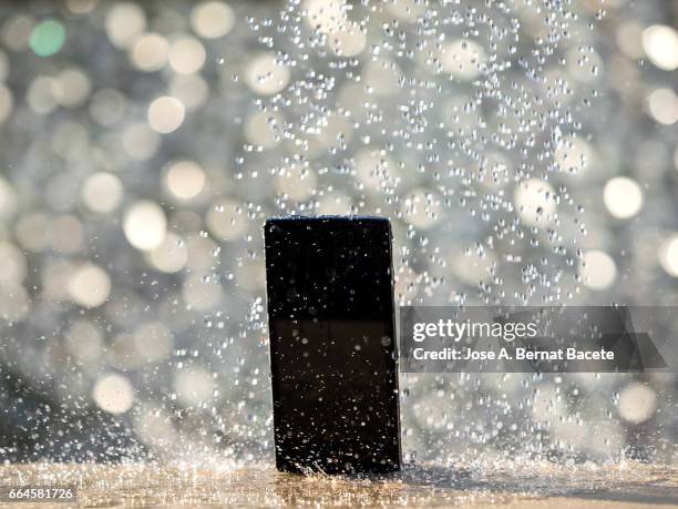 water jet striking on a wet mobile phone, outdoors illuminated by sunlight - enfoque diferencial photos et images de collection