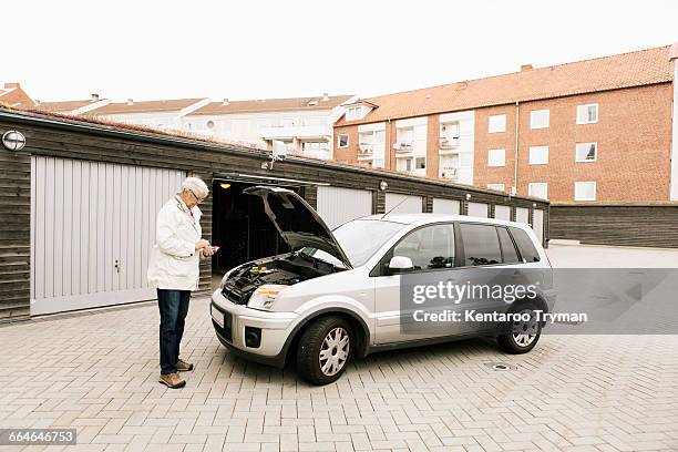 senior woman using phone while standing by broken down car - motorhaube stock-fotos und bilder