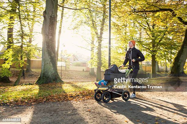 woman jogging with baby stroller on road at park - baby pram in the park stock pictures, royalty-free photos & images