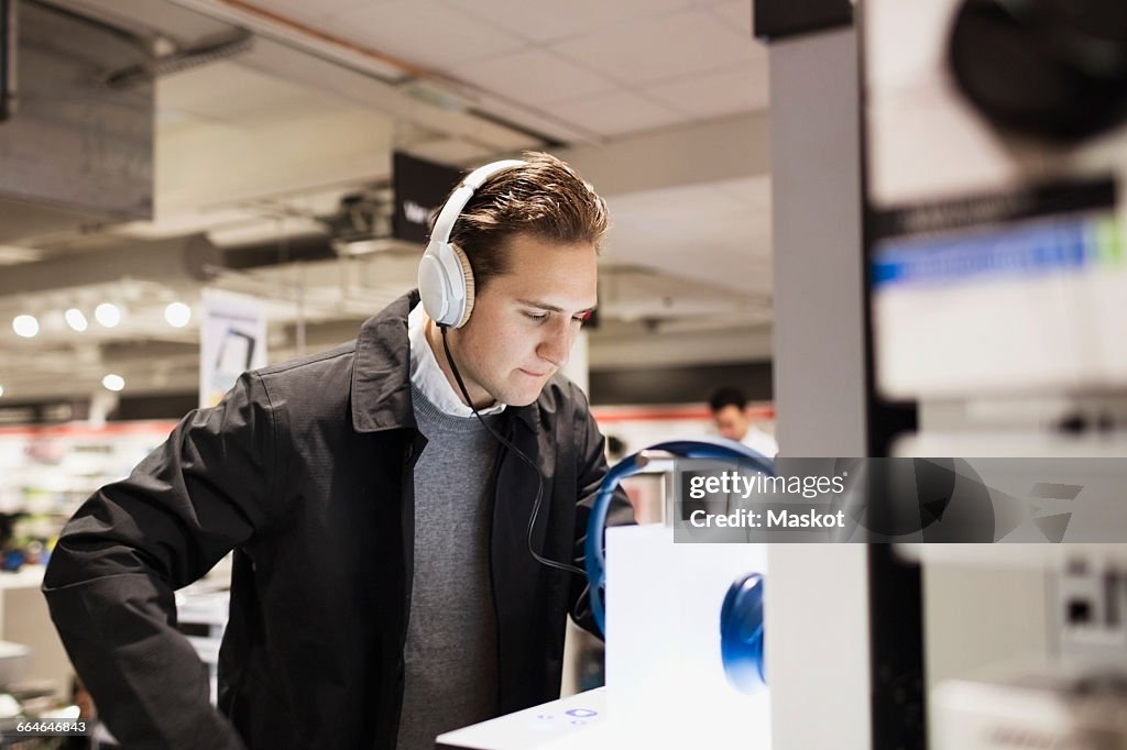 Male customer wearing headphones while standing in electronics store