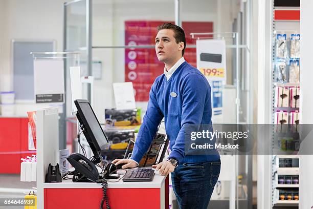 salesman looking up while standing at counter in store - caissière stockfoto's en -beelden