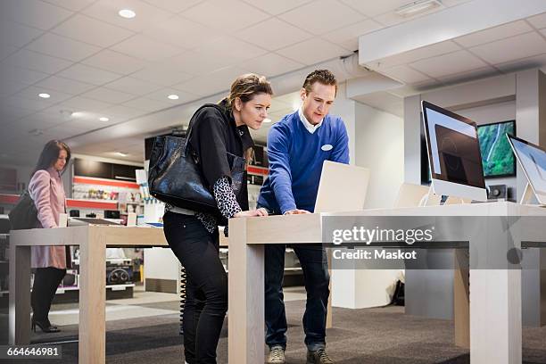 salesman assisting female customer in buying laptop at store - salesman fotografías e imágenes de stock