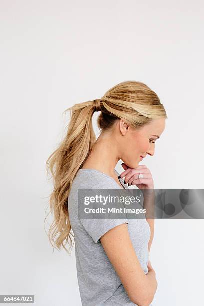 a young woman with blonde hair in a grey shirt, one hand on her chin. - queue de cheval photos et images de collection