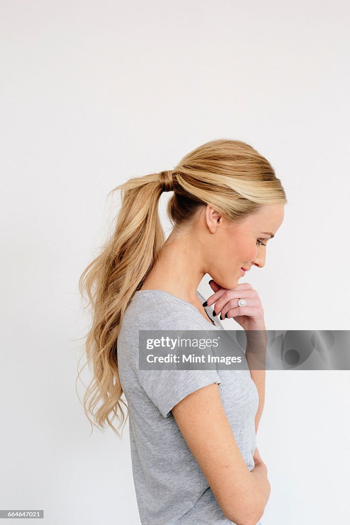 A young woman with blonde hair in a grey shirt, one hand on her chin.