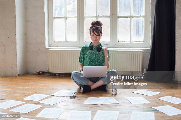 young woman sitting on the floor in a rehearsal studio, using a laptop computer, looking at sheet music. - sitting on ground stock pictures, royalty-free photos & images