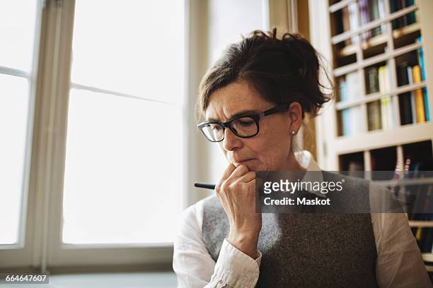 female professional with hand on chin by window in law library - serious interview stock pictures, royalty-free photos & images