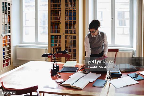 female professional holding book while standing at table in library - law library stock pictures, royalty-free photos & images