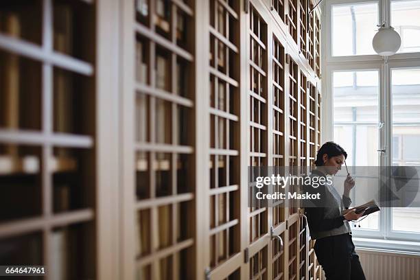 thoughtful female lawyer researching while leaning on shelf in library - law library stock pictures, royalty-free photos & images