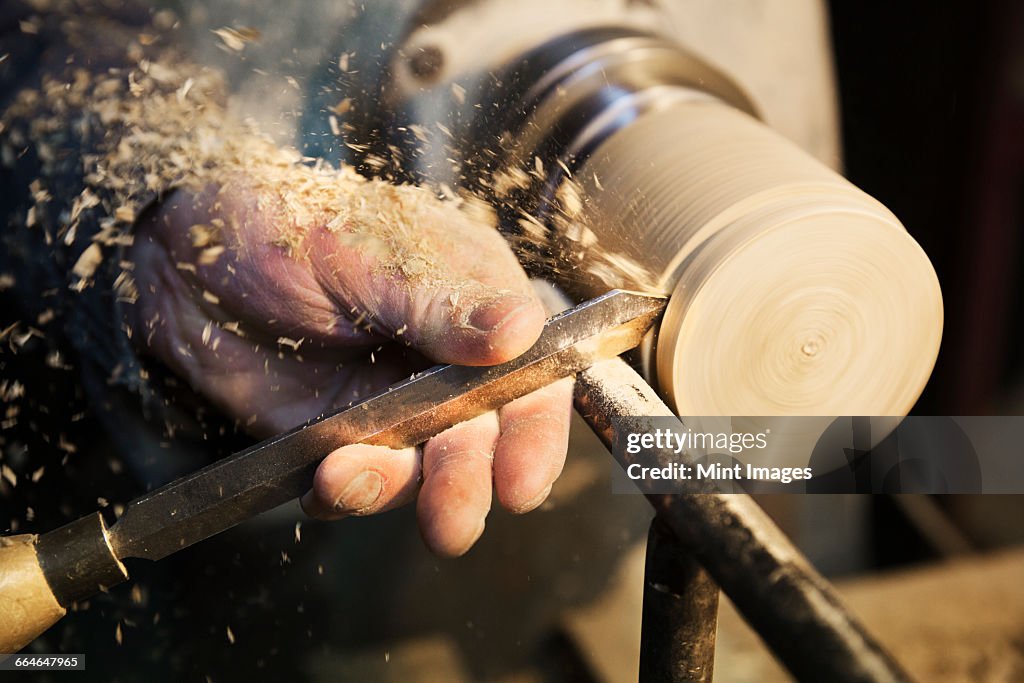 Man standing at a woodworking machine in a carpentry workshop, turning a piece of wood.