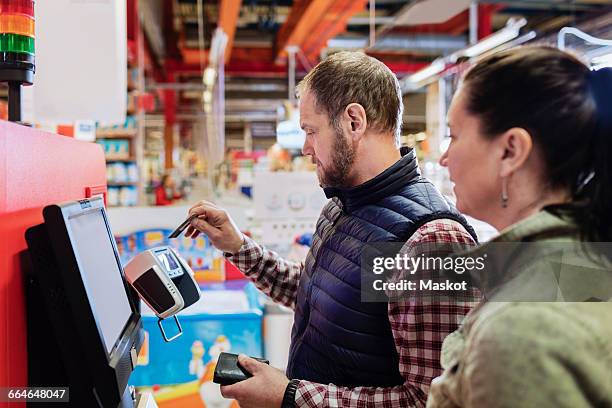 man paying with credit card while standing with woman at supermarket - paying supermarket foto e immagini stock