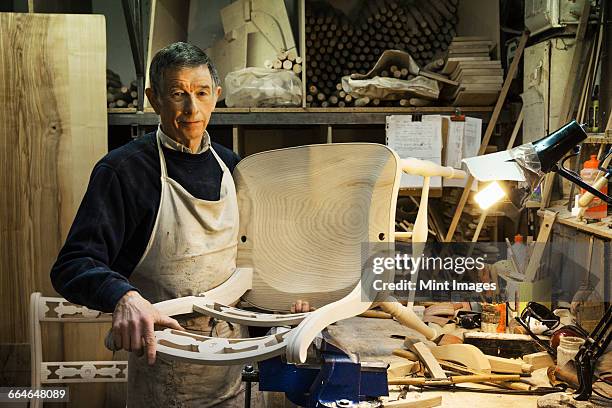 man standing at a work bench in a carpentry workshop, working on a wooden chair. - bench dedication stock pictures, royalty-free photos & images