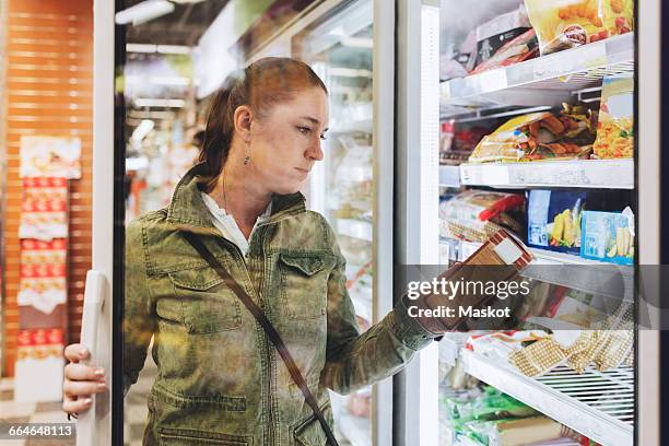 female customer reading product seen through glass door at refrigerated section - weekend activities stock pictures, royalty-free photos & images