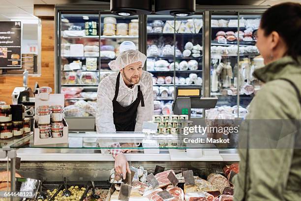 sales clerk looking at female customer while assisting at supermarket - delicatessen stock pictures, royalty-free photos & images