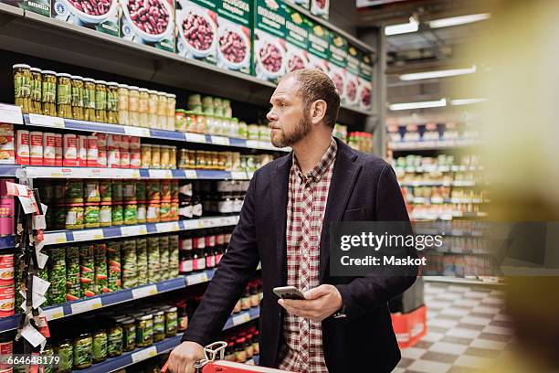 male customer holding smart phone while shopping in grocery store - shopping male foto e immagini stock