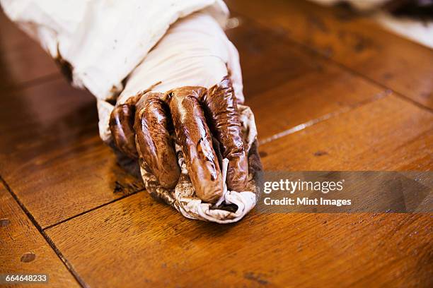 close up of a carpenter wearing protective gloves, applying varnish onto a wooden surface with a cloth. - wood stain stock pictures, royalty-free photos & images