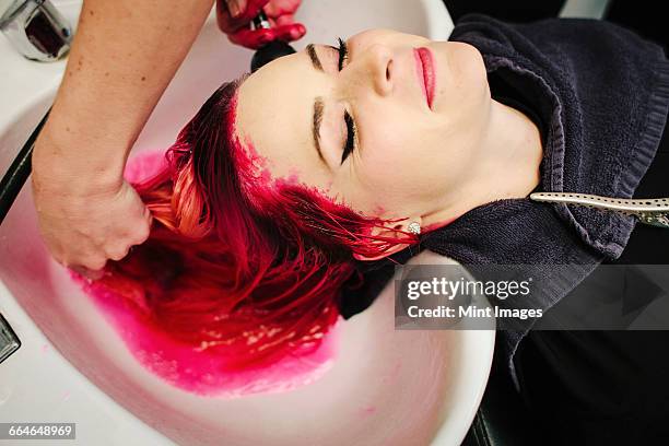 a hair salon client having red hair dye rinsed from her hair over a basin. - hair dye fotografías e imágenes de stock