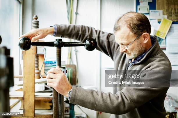 a man using a book press, winding the handle down to create pressure.  - old book side stock pictures, royalty-free photos & images