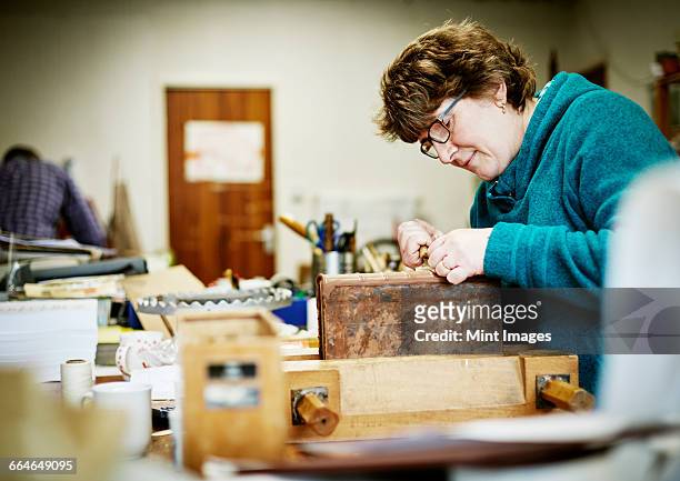 a woman working at a bench on the binding of a book in need of restoration. - reliures photos et images de collection