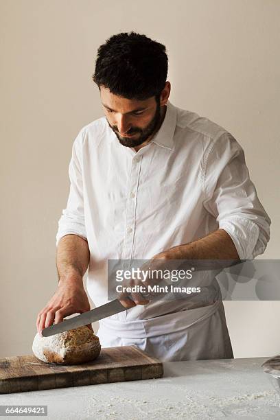 baker slicing a freshly baked loaf of bread with a bread knife. - bread knife stock pictures, royalty-free photos & images