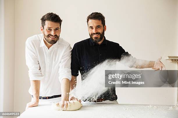 two bakers standing at a table, kneading bread dough, dusting it with flour. - family baking bread stock pictures, royalty-free photos & images