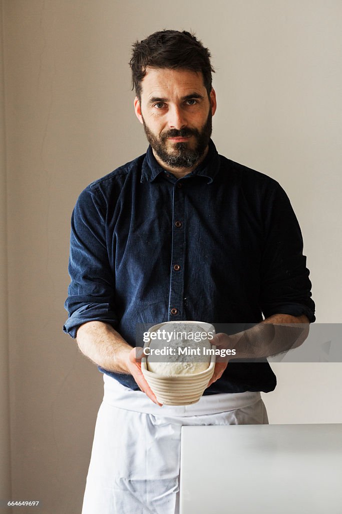 Baker holding a freshly baked loaf of white bread in a rattan proofing basket.