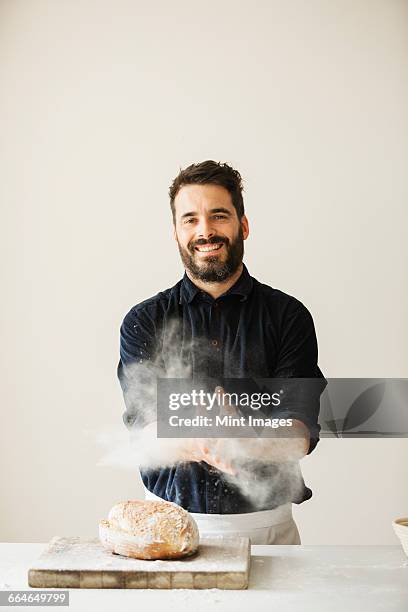 baker wiping his floury hands, a freshly baked loaf of bread on a chopping board. - beker stock pictures, royalty-free photos & images