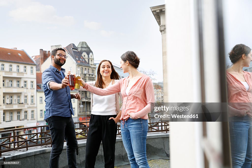 Man and two women clinking bottles on roof terrace