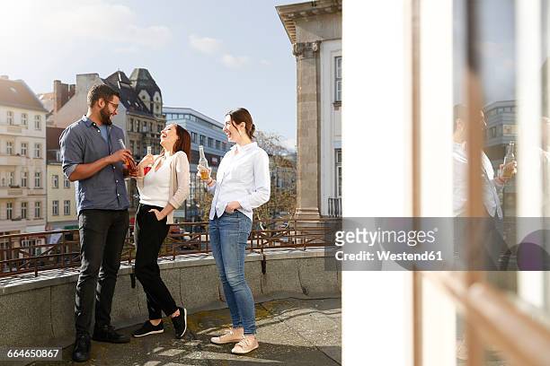 happy man and two women with bottles on roof terrace - blaue stunde stock-fotos und bilder