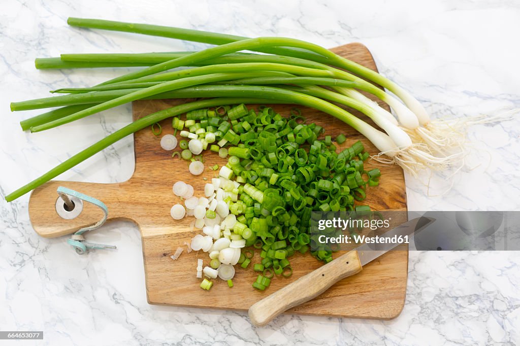 Chopped and whole spring onions on wooden board