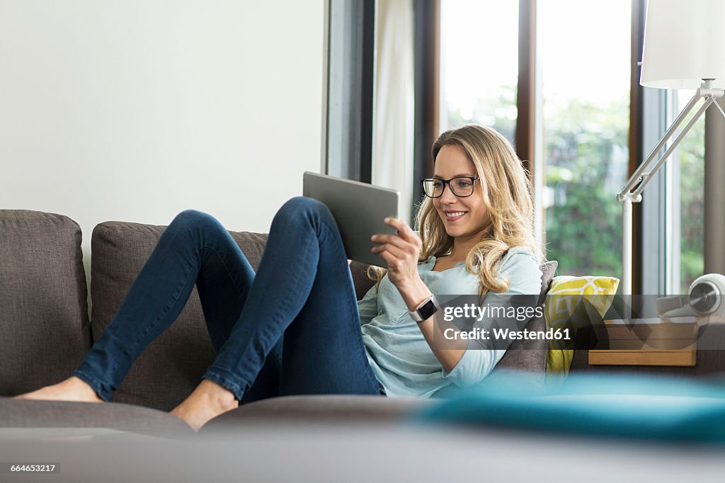 Smiling woman at home on couch using digital tablet