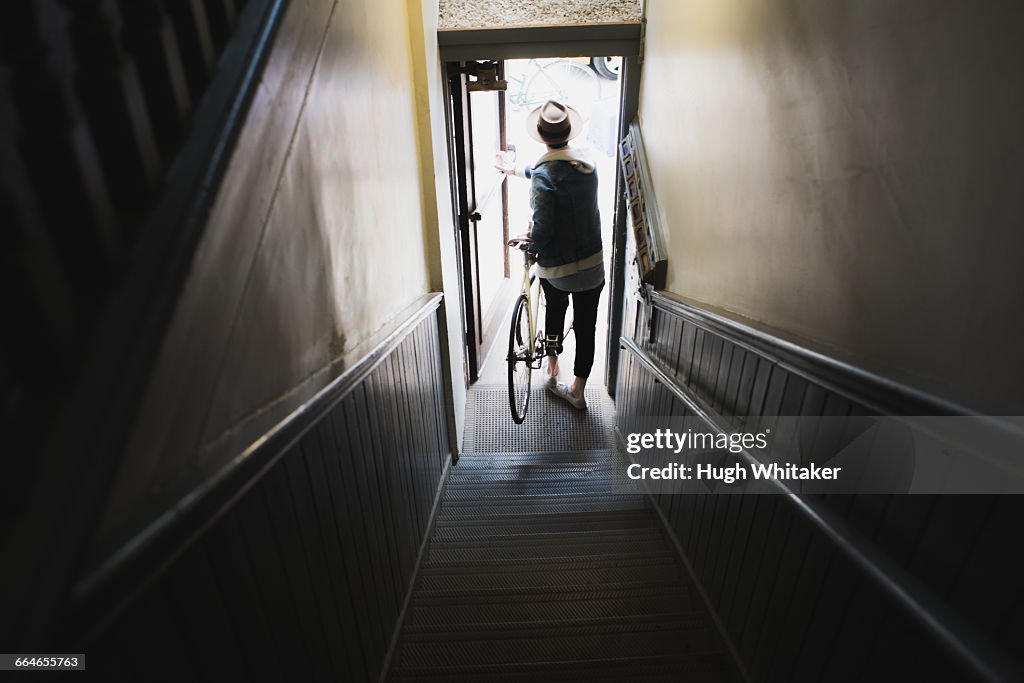 Young man at bottom of stairs, exiting building with bike, elevated view