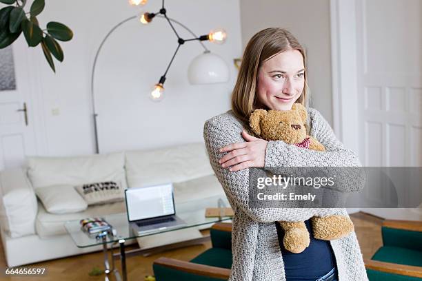 mid adult woman hugging teddy bear in living room - peluche foto e immagini stock