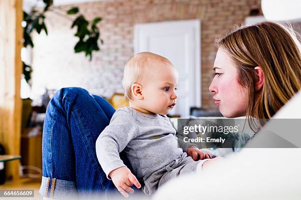 mid adult woman and baby daughter pulling faces on sofa - funny face baby stock pictures, royalty-free photos & images