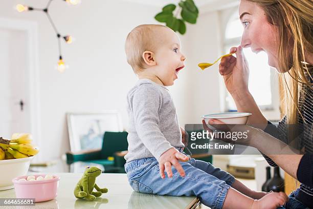 baby girl mimicking mother whilst eating at kitchen table - baby stock-fotos und bilder