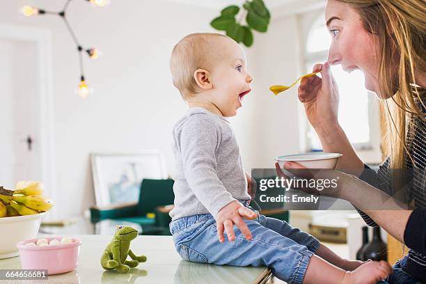 baby girl mimicking mother whilst eating at kitchen table - funny baby photo 個照片及圖片檔