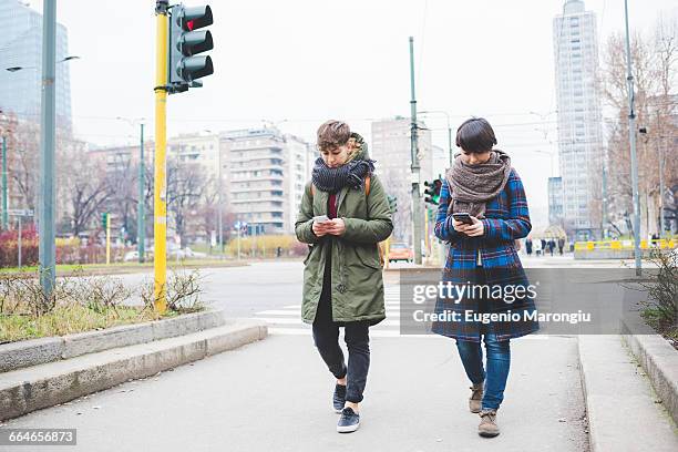 two sisters walking along street, using smartphones - geschwister frech stock-fotos und bilder