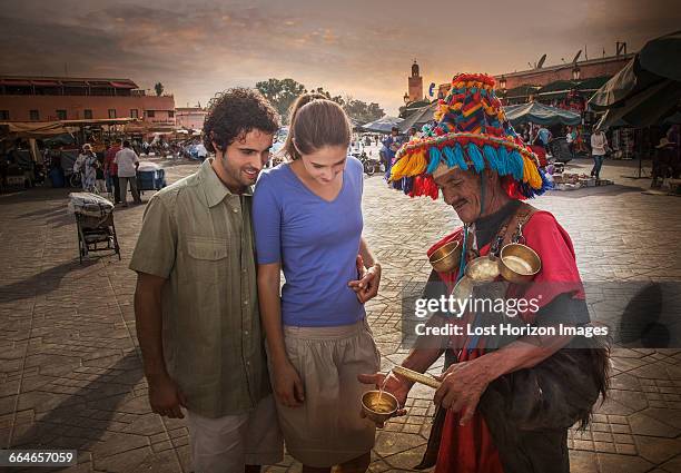 young couple chatting with market trader, jemaa el-fnaa square, marrakesh, morocco - marokko marrakesh stock-fotos und bilder