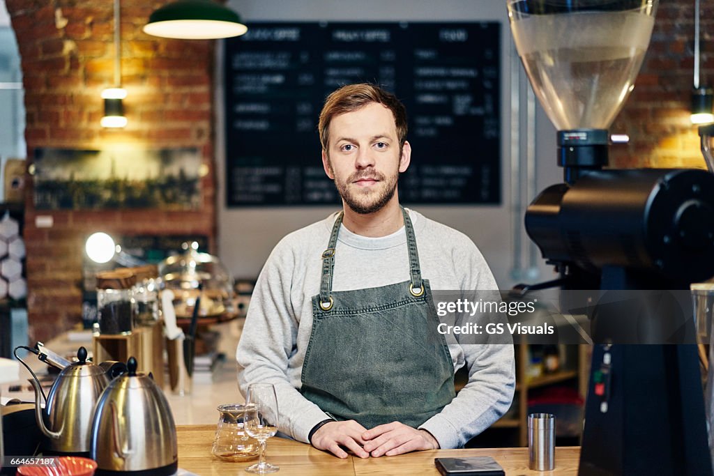 Portrait of young male barista at coffee shop kitchen counter
