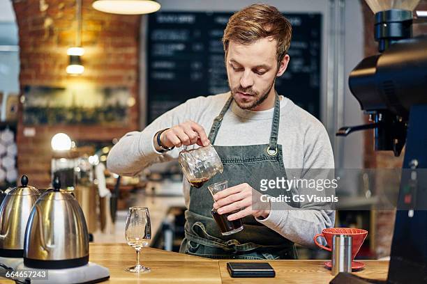 male barista pouring coffee at coffee shop kitchen counter - barista stock pictures, royalty-free photos & images